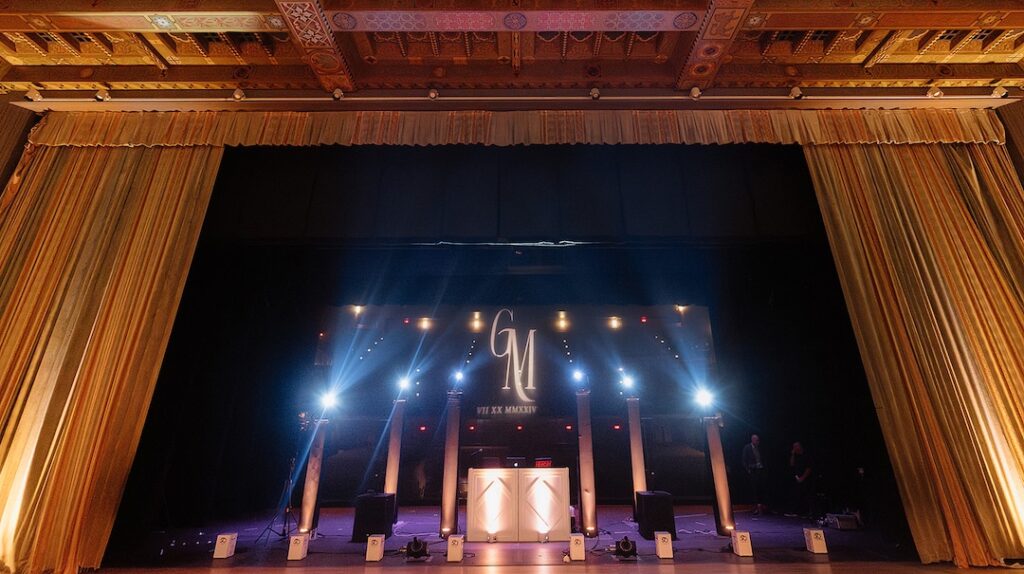 Elegant stage setup with dramatic lighting and gold curtains, featuring a central illuminated monogram.