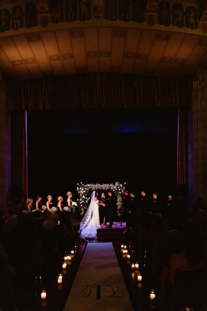 Bride and groom exchange vows under floral arch at elegant indoor wedding ceremony.