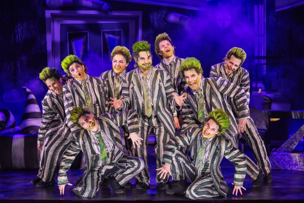 Performers in striped suits with green hair on stage in a vibrant theatrical production.