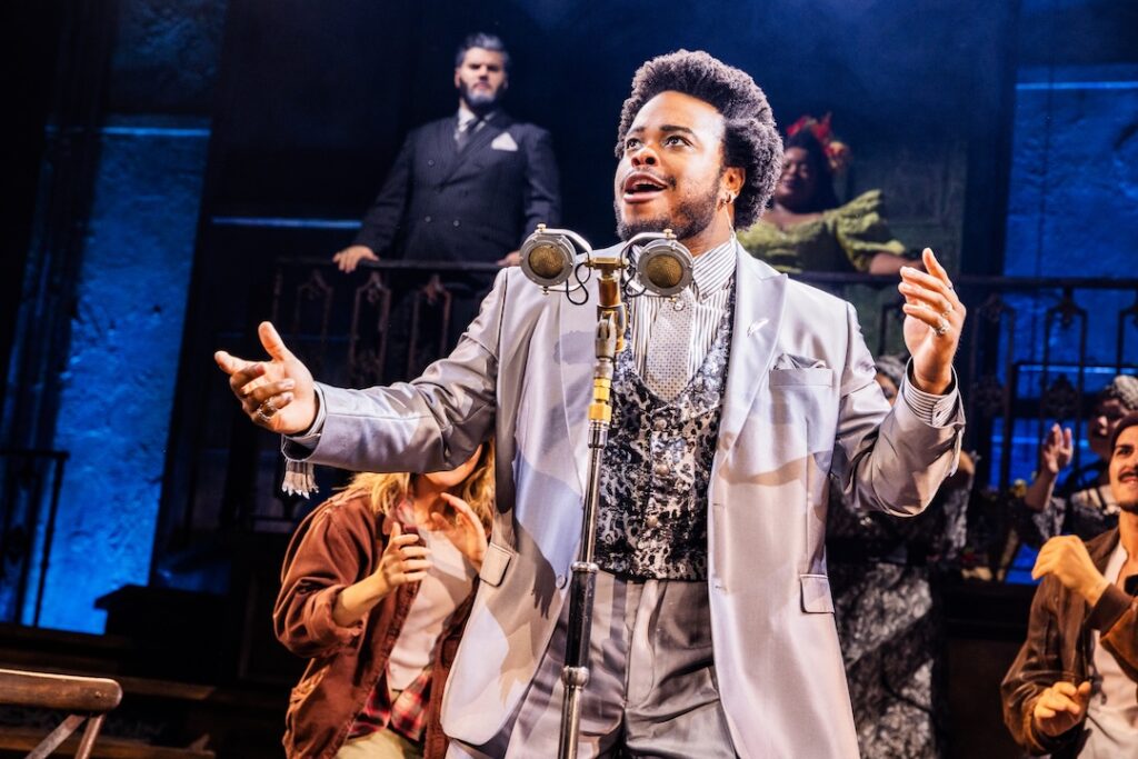 Performer in a suit singing passionately on stage during a theatrical production with an antique microphone.