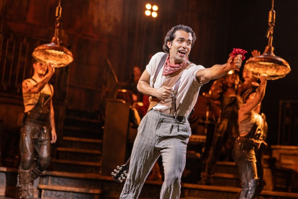 Performer enthusiastically offers a red flower on a lively theater stage.