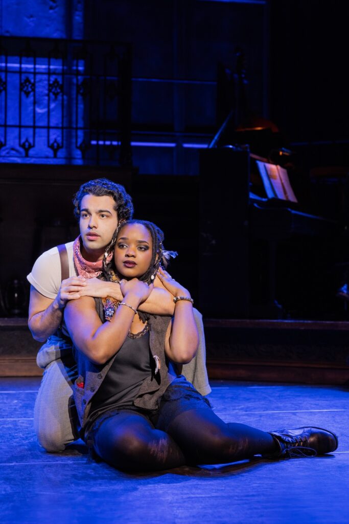 Two actors perform an emotional scene on stage, illuminated by blue lights in a theatrical setting.