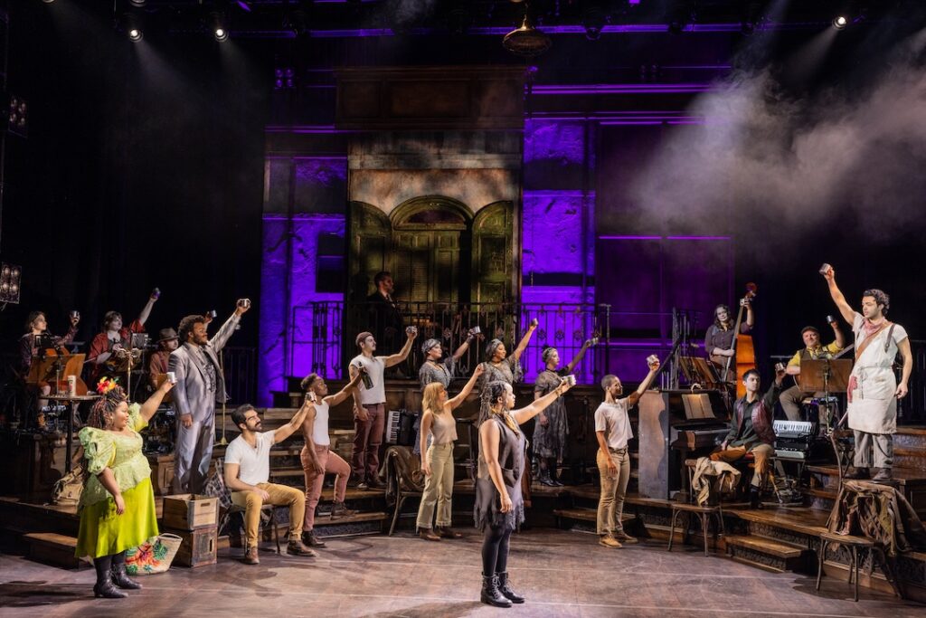 Performers on stage raising glasses in a lively theatrical production, vibrant lighting highlights the scene.